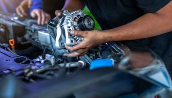 Mechanic is repairing and replacing a battery charger at car service center. Mechanic man holding alternator of the car in repair and maintenance garage.