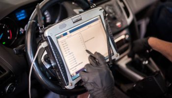 Automobile computer diagnosis. Car mechanic repairer looks for engine failure on diagnostics equipment in vehicle service workshop