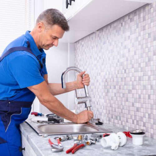 Side View Of A Plumber Fixing Water Tap In Kitchen